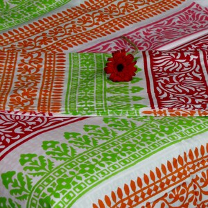 Pu&ograve; includere: Un tessuto bianco con strisce colorate di verde, arancione e rosa. Il tessuto presenta un motivo floreale ripetitivo. Un solo fiore rosa &egrave; posto sopra il tessuto.