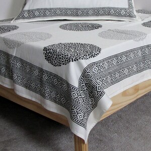 May include: White cotton bed sheet with a black and white geometric pattern. The sheet has a border of repeating geometric designs and a central design of circles with a floral pattern.