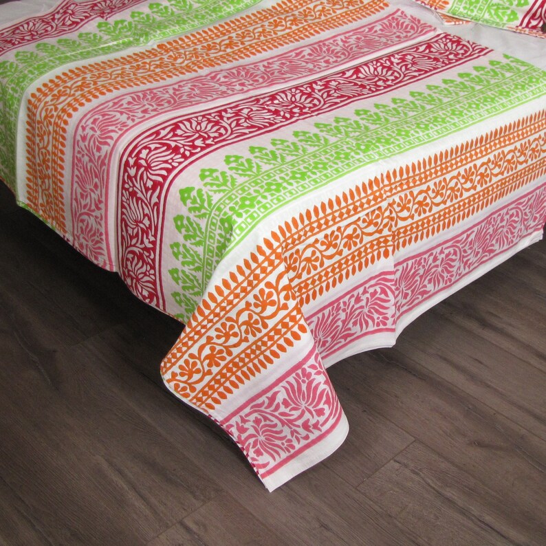 Pu&ograve; includere: Un copriletto in cotone bianco con strisce colorate e motivi floreali in tonalit&agrave; arancio, rosa, verde e rosso.