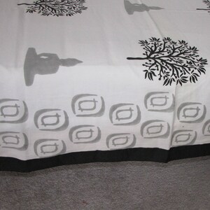 May include: White cotton fabric with a black and gray print of trees, a meditating figure, and geometric shapes. The fabric has a black border.