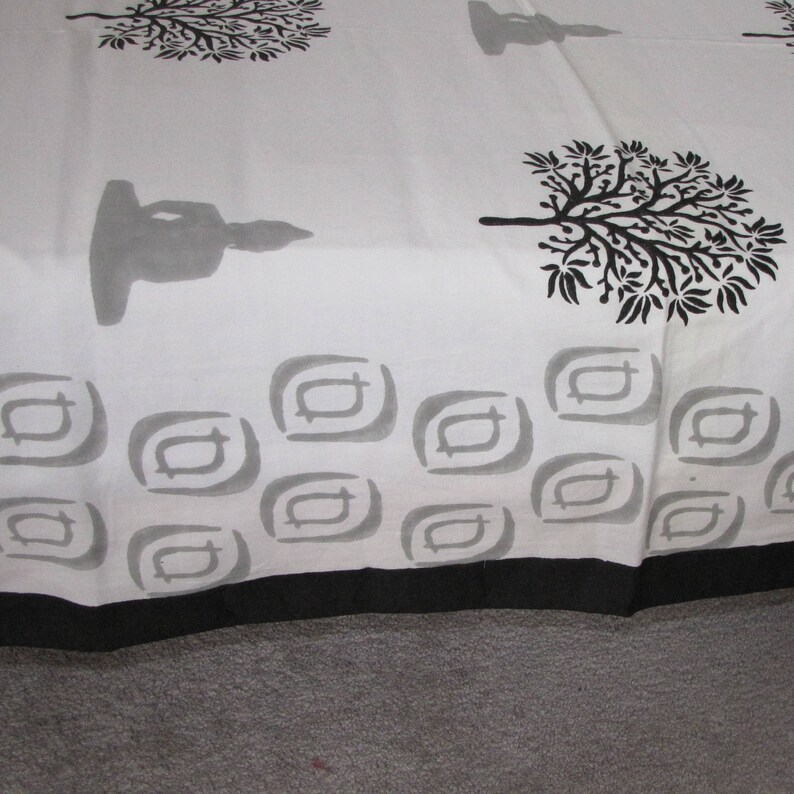 May include: White cotton fabric with a black and gray print of trees, a meditating figure, and geometric shapes. The fabric has a black border.