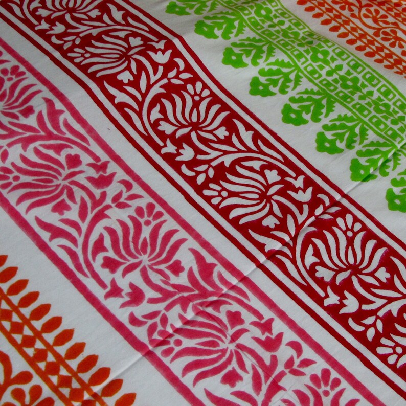Pu&ograve; includere: Tessuto bianco con strisce colorate di motivi floreali. Le strisce sono in tonalit&agrave; di arancione, rosa, rosso e verde.