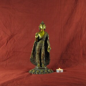 May include: A gold-coloured metal statue of Buddha standing on a lotus base. The statue is wearing a robe with intricate details and has a serene expression.