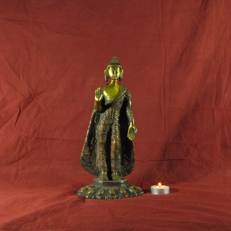 May include: A gold-coloured metal statue of Buddha standing on a lotus base. The statue is wearing a robe with intricate details and has a serene expression.