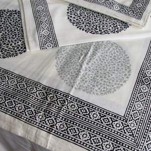 May include: White cotton fabric with a black and white geometric border and a black and white floral pattern. The fabric is folded in half, and the floral pattern is visible on both sides.