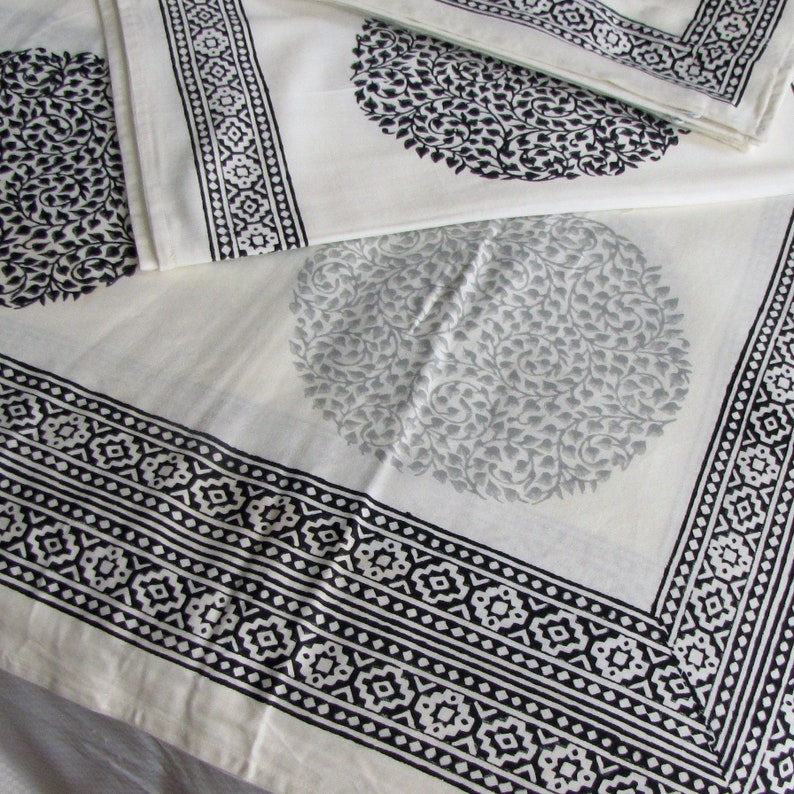 May include: White cotton fabric with a black and white geometric border and a black and white floral pattern. The fabric is folded in half, and the floral pattern is visible on both sides.