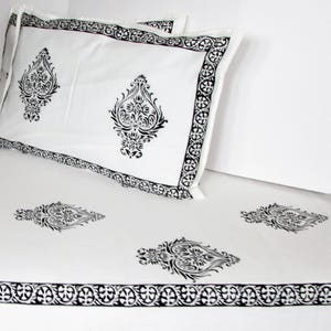 May include: White cotton bedding with a black and white paisley print. The bedding has a border of black and white paisley designs. The bedding is shown with two pillowcases.