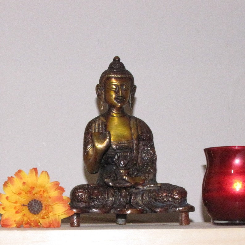 May include: A gold-toned brass statue of a seated Buddha with a serene expression. The statue is on a wooden base and has intricate details.