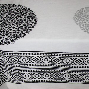May include: Black and white fabric with a repeating geometric pattern along the bottom edge. The fabric has two large circular designs with a floral pattern.