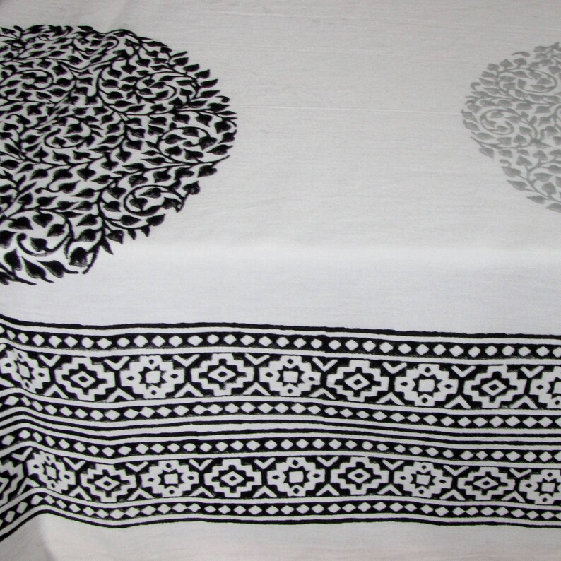 May include: Black and white fabric with a repeating geometric pattern along the bottom edge. The fabric has two large circular designs with a floral pattern.