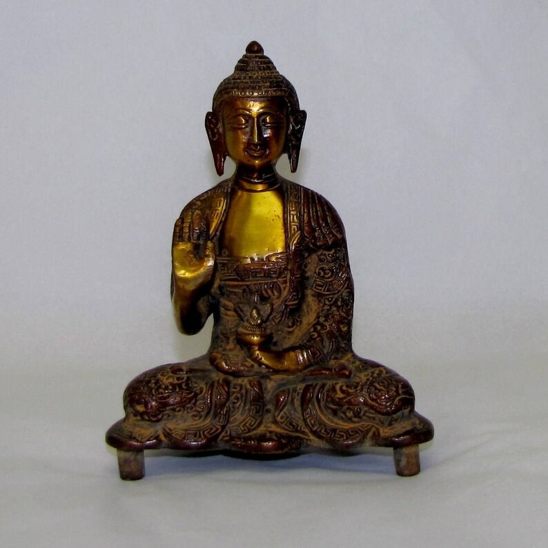 May include: A gold-colored metal statue of a seated Buddha with intricate details on the robe and base. The Buddha has a serene expression and is in a meditative pose.