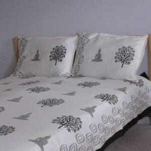 May include: White cotton bedding with a black and gray print of trees and a meditating Buddha. The bedding is on a bed with a wooden headboard.