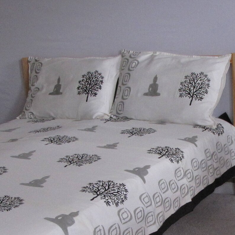 May include: White cotton bedding with a black and gray print of trees and a meditating Buddha. The bedding is on a bed with a wooden headboard.