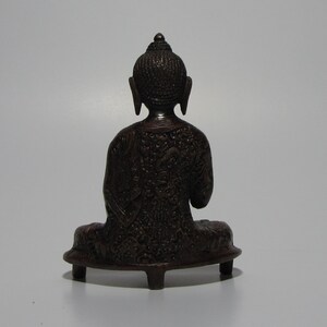 May include: A dark brown, intricately carved, seated Buddha statue with a small, rounded base.