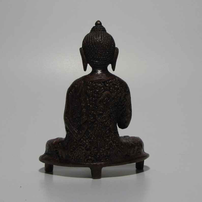 May include: A dark brown, intricately carved, seated Buddha statue with a small, rounded base.