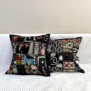 Peut inclure: Deux coussins de décoration en patchwork noir avec des broderies colorées et des paillettes. Les coussins sont sur un canapé blanc.