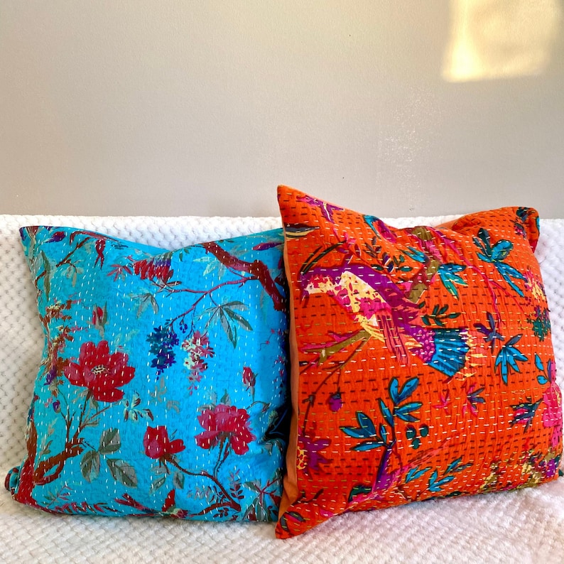 May include: Two decorative throw pillows with floral patterns. One pillow is turquoise blue with pink and white flowers, the other is orange with pink and blue birds.