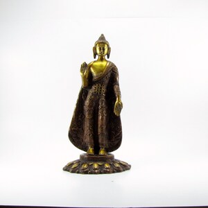May include: A gold and brown metal statue of Buddha standing on a lotus base. The statue is in a meditative pose with one hand raised in a gesture of blessing.