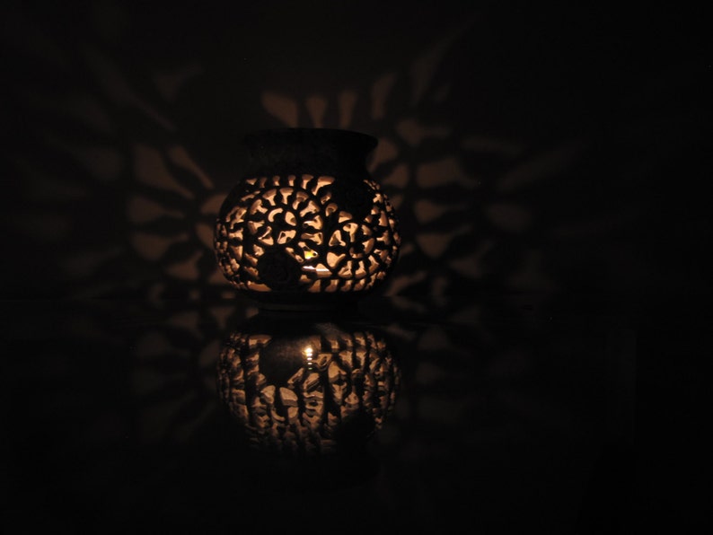 May include: A white ceramic candle holder with intricate floral designs. The candle holder is lit and casting shadows on the surface.