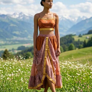 Könnte beinhalten: Ein zweiteiliges Outfit mit einem Crop-Top und einem langen Rock. Das Crop-Top ist in einem gebrannten Orange mit goldenen Verzierungen gehalten, der Rock hat ein Patchwork-Design in Orange- und Rosatönen. Das Outfit wird mit braunen Sandalen getragen.