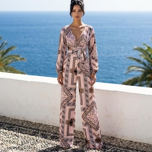 May include: A long-sleeved jumpsuit featuring a light pink base with a dark brown and black geometric and paisley-inspired pattern. The garment has a deep V-neckline, a cinched waist with a tie-front detail, and wide-leg trousers that fall to the floor.