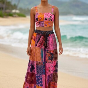 Op de afbeelding: Een tweedelige patchwork-outfit met een crop top en een maxi-rok. De top heeft een vierkante halslijn en brede bandjes, terwijl de rok een vloeiend, gelaagd ontwerp is. De outfit toont een mix van bloemen- en geometrische patronen in roze, oranje en paarse tinten.