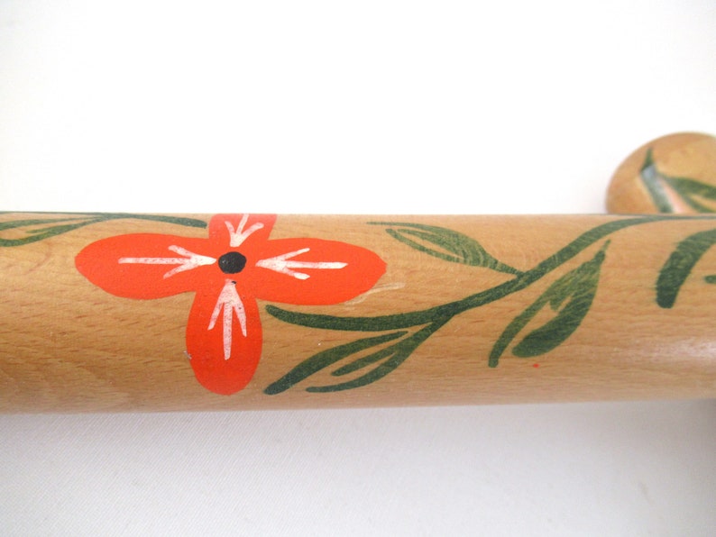 Puede incluir: Un rodillo de madera con un dise&ntilde;o pintado a mano de hojas verdes y una flor roja con un centro negro.