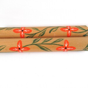 Puede incluir: Dos rodillos de amasar de madera con un dise&ntilde;o floral. Los rodillos de amasar est&aacute;n pintados con hojas verdes y flores naranjas.