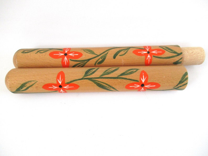 Puede incluir: Dos rodillos de amasar de madera con un dise&ntilde;o floral. Los rodillos de amasar est&aacute;n pintados con hojas verdes y flores naranjas.