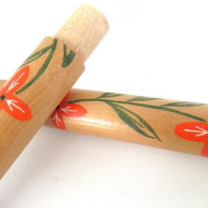 Puede incluir: Dos rodillos de amasar de madera con un dise&ntilde;o floral. Los rodillos de amasar est&aacute;n pintados con hojas verdes y flores naranjas.