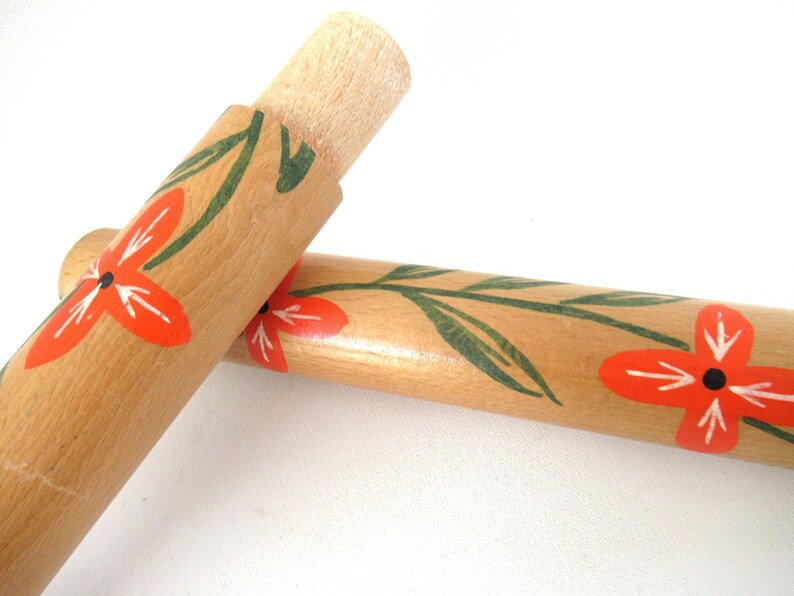 Puede incluir: Dos rodillos de amasar de madera con un dise&ntilde;o floral. Los rodillos de amasar est&aacute;n pintados con hojas verdes y flores naranjas.