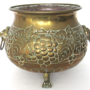 Può includere: Un grande vaso in ottone con un designo a vite. Il vaso ha due maniglie a testa di leone e tre piedi.