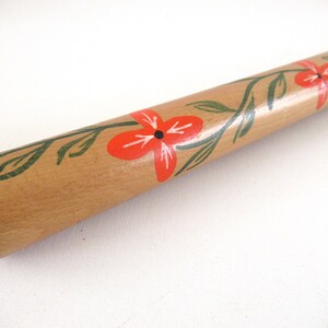 Puede incluir: Un rodillo de madera con un dise&ntilde;o pintado a mano de flores rojas y hojas verdes.