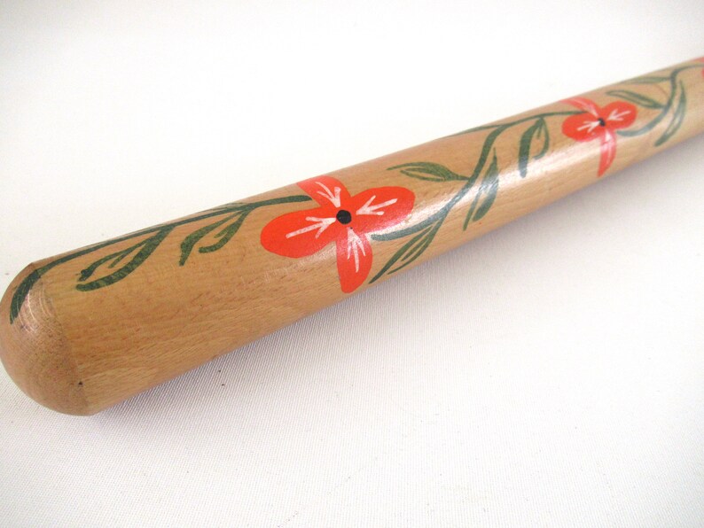 Puede incluir: Un rodillo de madera con un dise&ntilde;o pintado a mano de flores rojas y hojas verdes.