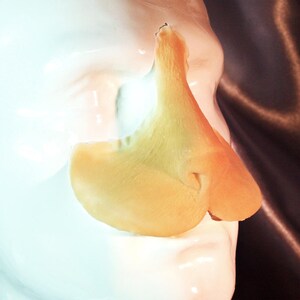 Peut inclure: Gros plan sur un mod&egrave;le anatomique de nez de couleur claire. Le mod&egrave;le est de couleur jaune p&acirc;le et semble &ecirc;tre fait d'un mat&eacute;riau lisse. Le nez est positionn&eacute; sur une surface blanche, avec un fond sombre.