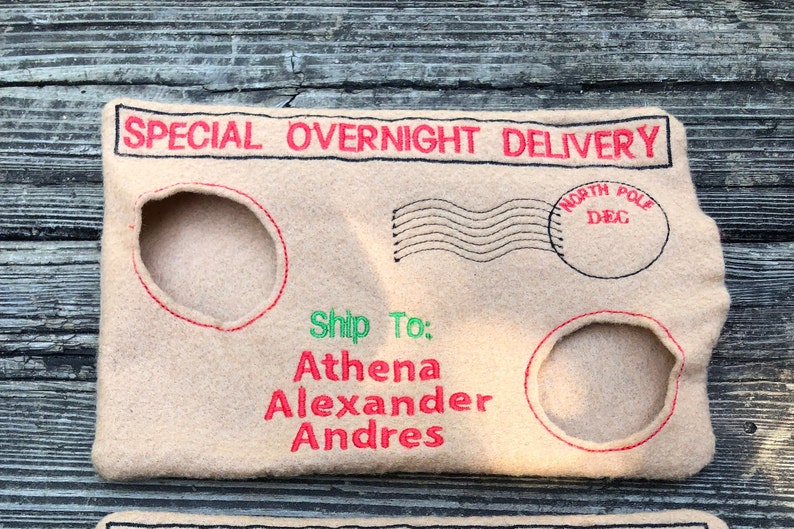 May include: A beige felt envelope with red and black embroidered details. The text "SPECIAL OVERNIGHT DELIVERY" is at the top. It has two circular cutouts and the text "Ship To: Athena Alexander Andres" in red and green.