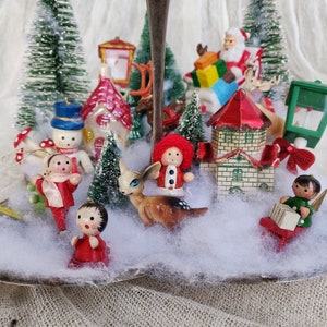 May include: A Christmas-themed display on a silver serving tray, featuring miniature figurines and bottle brush trees. The scene includes Santa Claus, reindeer, houses, snowmen, and other festive ornaments, creating a charming winter wonderland.