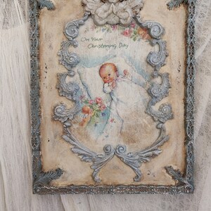 May include: A vintage-style framed artwork with a baby illustration, angel, and floral accents. The frame is distressed with a blue-gray finish. The artwork includes the text "On Your Christening Day".