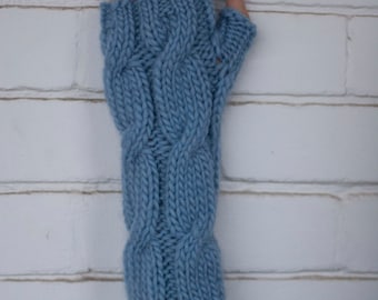 May include: A light blue cable-knit fingerless glove. The glove is made of a soft, textured yarn and features a braided cable design. The glove covers the hand and wrist, leaving the fingers exposed.