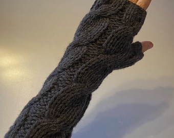 May include: Dark gray cable-knit fingerless gloves. The gloves are made of a thick, textured yarn and feature a classic cable-knit design. The gloves cover the hand and wrist, leaving the fingers free.