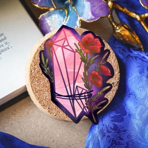 May include: A sticker featuring a pink geometric crystal shard wrapped in dark purple lines, accompanied by vibrant red poppy flowers with green stems and leaves, set against a deep purple background with a subtle starry pattern.