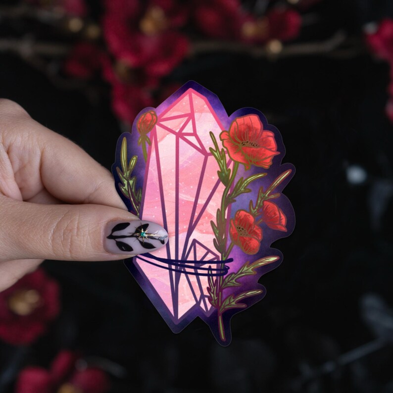 May include: A die-cut sticker featuring a large, multifaceted pink crystal cluster intertwined with vibrant red poppy flowers and green stems, set against a dark purple and black background with a subtle starry texture throughout the design.