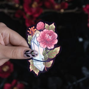 May include: A die-cut sticker featuring a central white crystal point wrapped in a dark string, surrounded by pink peony flowers and green leaves. The illustration is set against a dark background, showcasing detailed botanical and mineral elements.