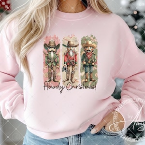 May include: Pink sweatshirt with a graphic of three nutcracker figures wearing cowboy hats and the text "Howdy Christmas!"