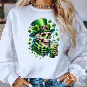 Op de afbeelding: Wit sweatshirt met een groene en witte schedel die een groene leprechaun-hoed draagt en een groen en wit ijsdrankje vasthoudt. De schedel is omringd door groene klaverblaadjes.