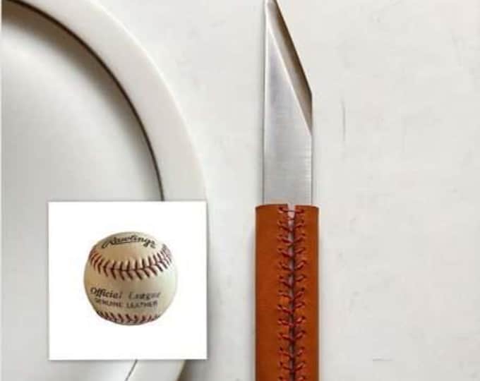 The Le Tranchet table knife, BASEBALL version, is a steak knife with an asymmetrical blade and a leather handle.