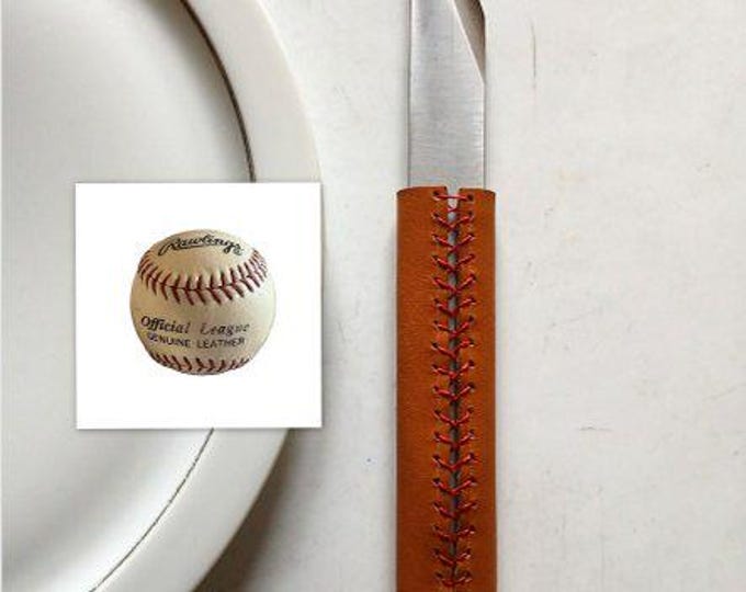 The Le Tranchet table knife, BASEBALL version, is a steak knife with an asymmetrical blade and a leather handle.