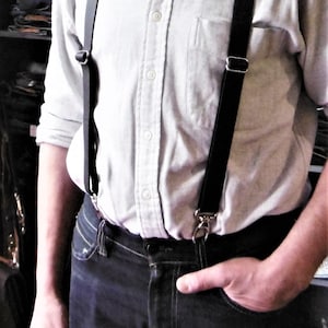 Peut inclure: Un homme portant une chemise blanche boutonnée avec des bretelles noires et un jean bleu foncé.