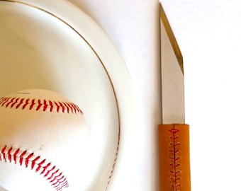 The Le Tranchet table knife, BASEBALL version, is a steak knife with an asymmetrical blade and a leather handle.