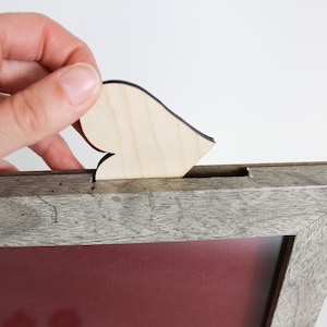 Op de afbeelding: Een houten fotolijst met een grijze verweerde afwerking. Een klein houten hartje wordt in een gleuf aan de bovenkant van de lijst geplaatst.